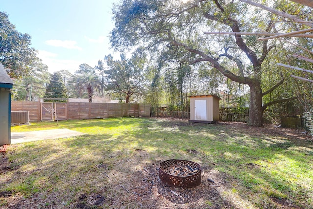 view of yard with a fenced backyard, central AC unit, a fire pit, and an outdoor structure