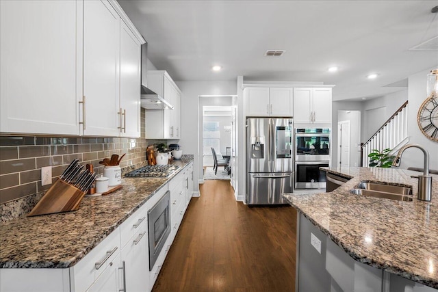 kitchen featuring a sink, appliances with stainless steel finishes, wall chimney range hood, decorative backsplash, and dark wood-style flooring