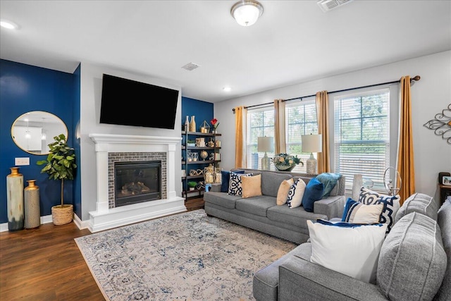 living area with visible vents, baseboards, dark wood-style flooring, and a tiled fireplace