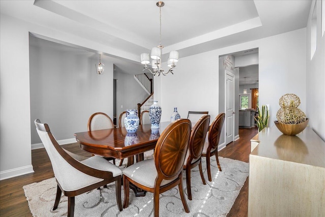 dining area with a tray ceiling, wood finished floors, baseboards, a chandelier, and stairs