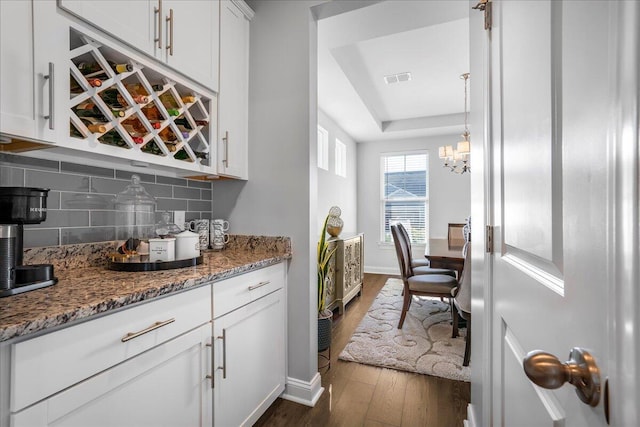 bar with tasteful backsplash, visible vents, dark wood finished floors, a notable chandelier, and a raised ceiling