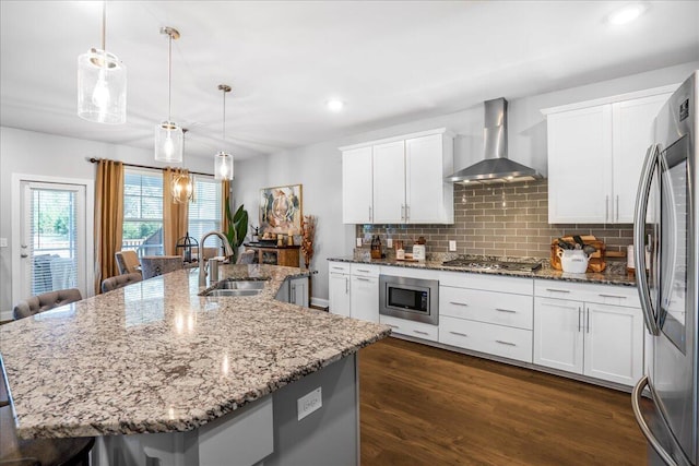 kitchen with dark wood-style floors, a sink, appliances with stainless steel finishes, wall chimney range hood, and tasteful backsplash