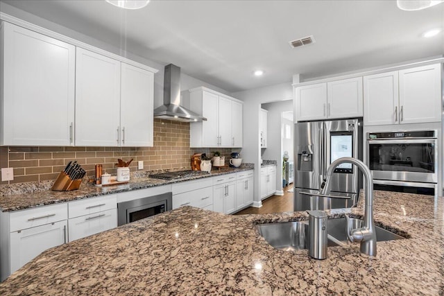 kitchen with visible vents, a sink, appliances with stainless steel finishes, wall chimney exhaust hood, and backsplash