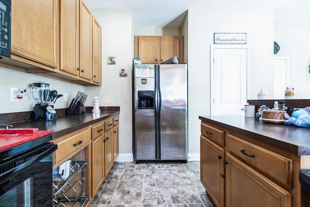 kitchen featuring brown cabinets, stainless steel refrigerator with ice dispenser, dark countertops, black microwave, and baseboards