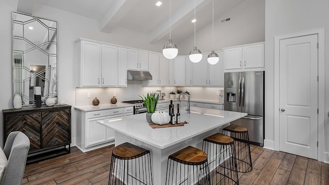 kitchen featuring dark hardwood / wood-style flooring, appliances with stainless steel finishes, beamed ceiling, a kitchen island with sink, and tasteful backsplash