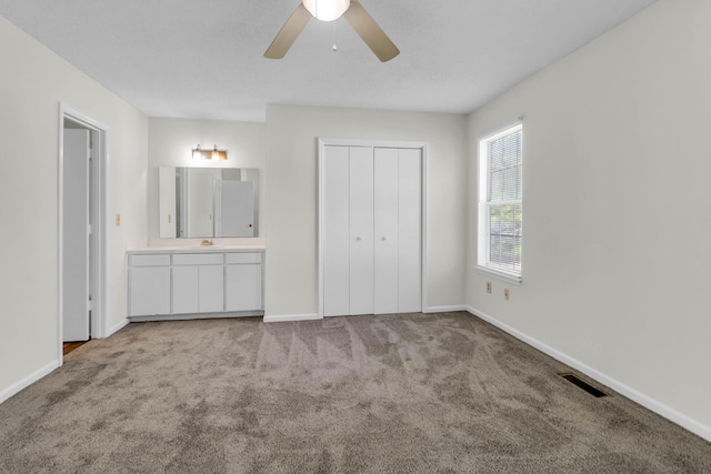 unfurnished bedroom with light carpet, ensuite bath, ceiling fan, and a closet