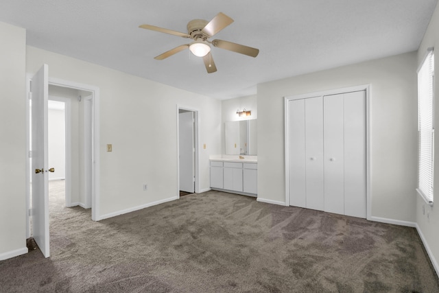 unfurnished bedroom with dark colored carpet, multiple windows, and connected bathroom