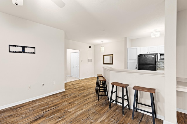 kitchen featuring black refrigerator, dark hardwood / wood-style floors, white cabinetry, and tasteful backsplash