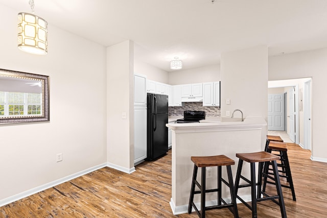 kitchen featuring black appliances, white cabinets, light wood-type flooring, decorative light fixtures, and kitchen peninsula