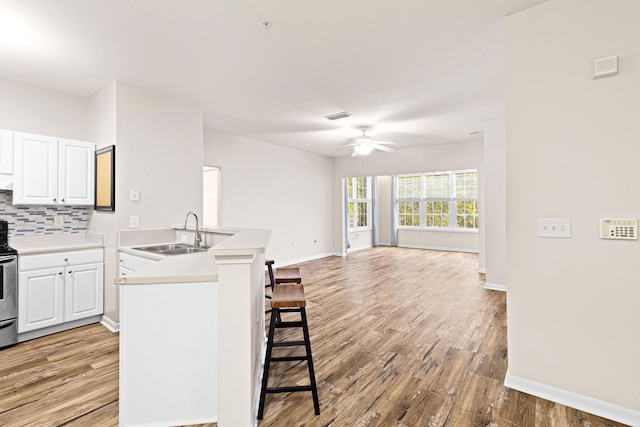 kitchen with sink, white cabinetry, light hardwood / wood-style floors, a kitchen bar, and kitchen peninsula