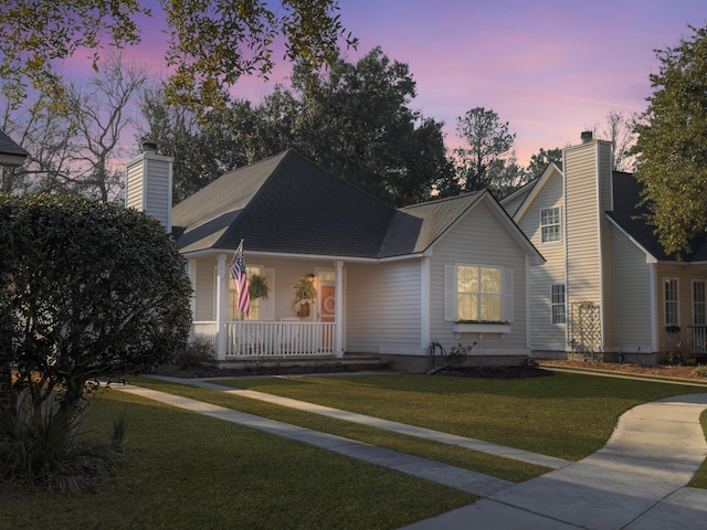 view of front of property featuring a porch, roof with shingles, a lawn, and a chimney