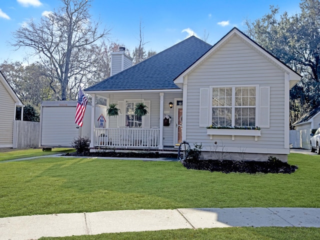 view of front facade with covered porch, a shingled roof, a chimney, and a front lawn