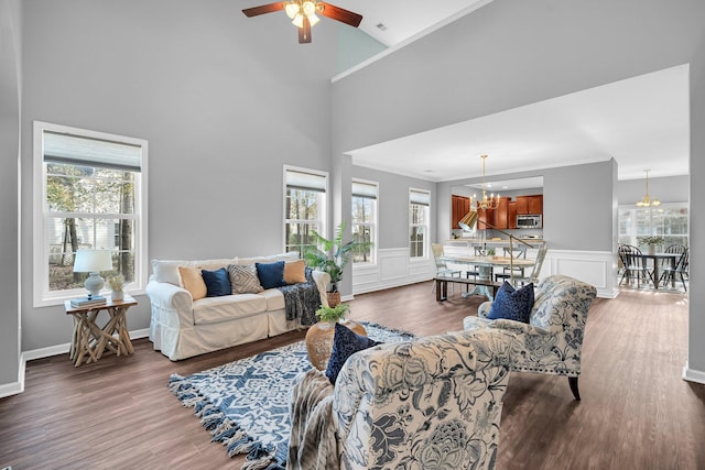 living room featuring hardwood / wood-style flooring, ornamental molding, a towering ceiling, and ceiling fan with notable chandelier