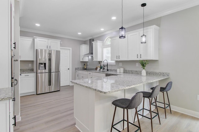 kitchen featuring stainless steel fridge, light wood-style floors, wall chimney exhaust hood, a peninsula, and ornamental molding