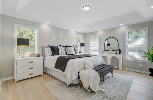 bedroom with a tray ceiling, multiple windows, and light wood-type flooring