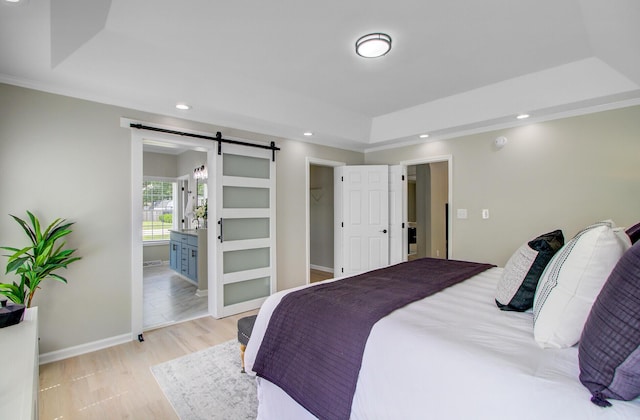 bedroom with a barn door, recessed lighting, baseboards, a raised ceiling, and ensuite bath