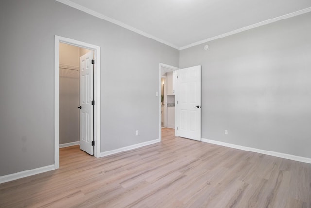 unfurnished bedroom with crown molding, baseboards, a walk in closet, and light wood finished floors