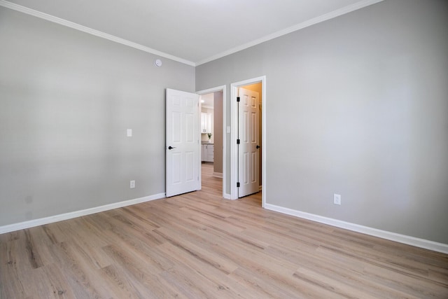 empty room with crown molding, baseboards, and light wood finished floors