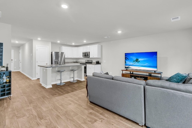 living area with baseboards, light wood-style flooring, visible vents, and recessed lighting