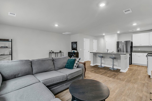 living room with light wood finished floors, baseboards, visible vents, and recessed lighting