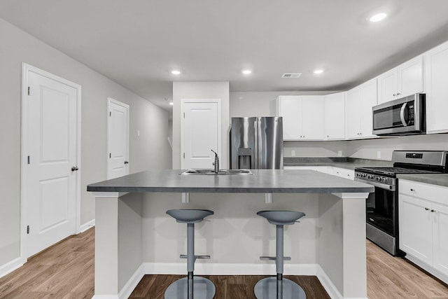 kitchen featuring visible vents, dark countertops, wood finished floors, stainless steel appliances, and a sink