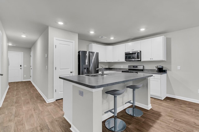 kitchen featuring light wood finished floors, visible vents, dark countertops, appliances with stainless steel finishes, and a sink