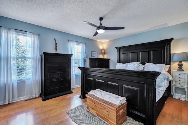 bedroom featuring light wood-style flooring, a ceiling fan, visible vents, and a textured ceiling