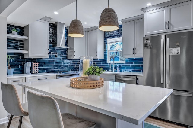 kitchen featuring wall chimney range hood, decorative light fixtures, a kitchen bar, stainless steel appliances, and a sink