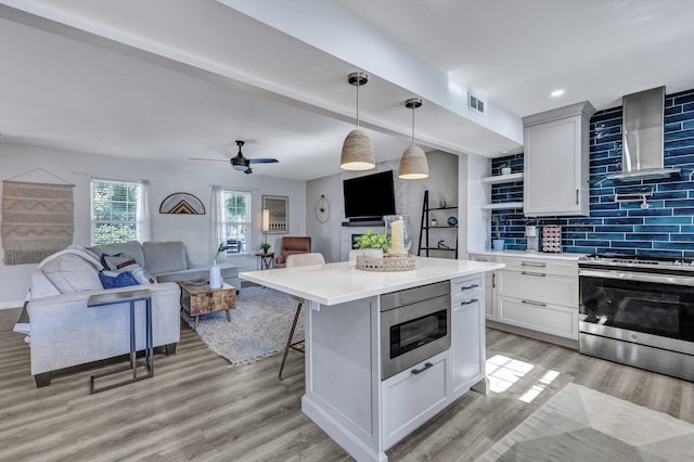 kitchen featuring visible vents, wall chimney range hood, open floor plan, stainless steel appliances, and light countertops