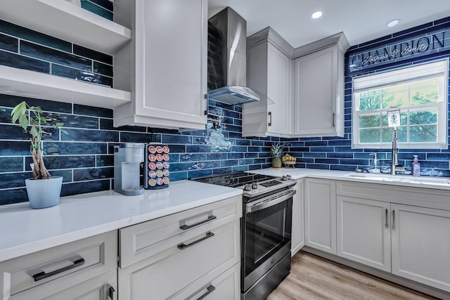 kitchen featuring light countertops, wall chimney range hood, stainless steel range with electric stovetop, and a sink