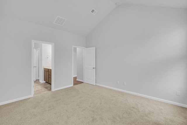 unfurnished bedroom with high vaulted ceiling, connected bathroom, and light colored carpet