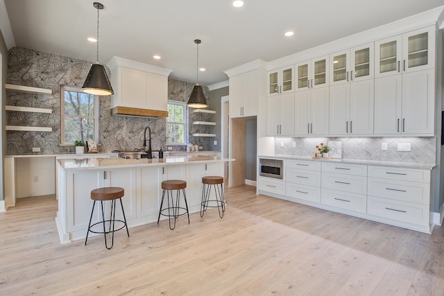 kitchen with light wood-type flooring, white cabinetry, pendant lighting, and a kitchen island with sink