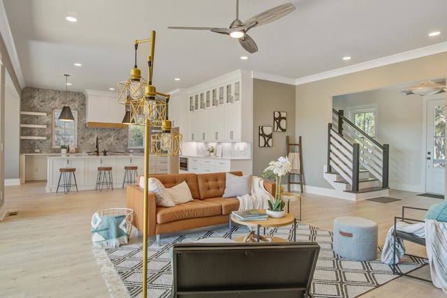 living room with light wood-type flooring, ceiling fan, ornamental molding, and indoor wet bar