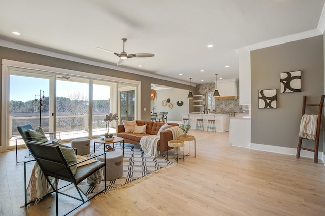 living room with sink, ceiling fan, light wood-type flooring, and ornamental molding