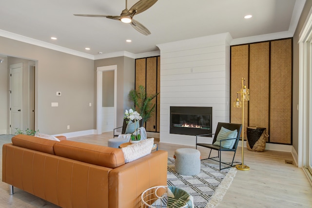 living room featuring light wood-type flooring, ceiling fan, ornamental molding, and a fireplace