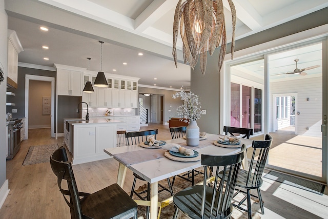 dining space featuring sink, light wood-type flooring, beamed ceiling, ceiling fan, and ornamental molding