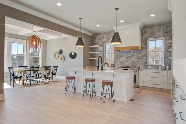 kitchen with high end stainless steel range oven, an island with sink, light wood-type flooring, white cabinetry, and a kitchen bar