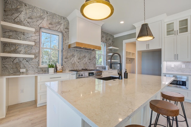 kitchen featuring an island with sink, white cabinets, light stone counters, and pendant lighting