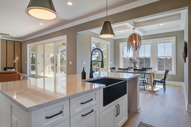 kitchen with a center island with sink, hanging light fixtures, light stone counters, sink, and white cabinetry