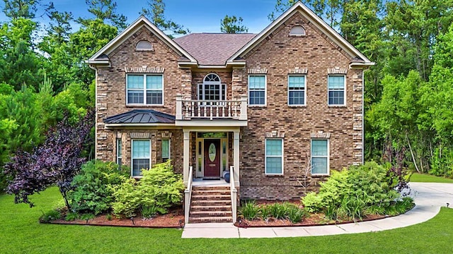 view of front of house with a balcony, a standing seam roof, a front lawn, and brick siding