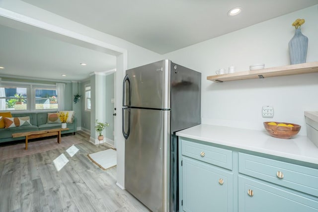 kitchen with light hardwood / wood-style floors, crown molding, and stainless steel refrigerator