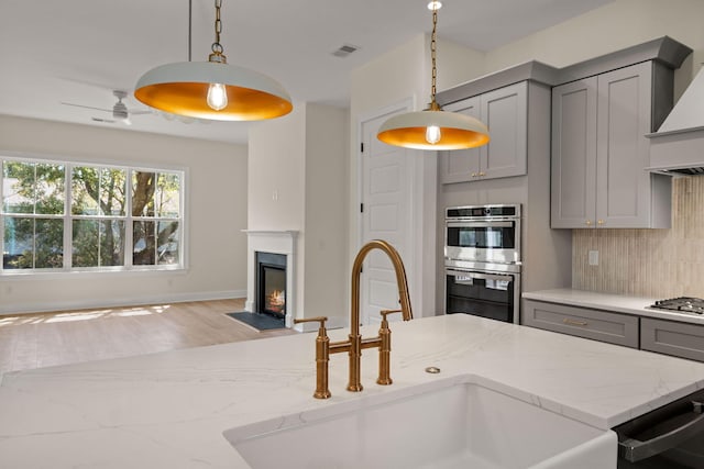 kitchen with gray cabinetry, a sink, backsplash, and appliances with stainless steel finishes