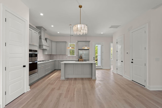 kitchen featuring decorative backsplash, premium range hood, appliances with stainless steel finishes, light wood-style floors, and gray cabinets