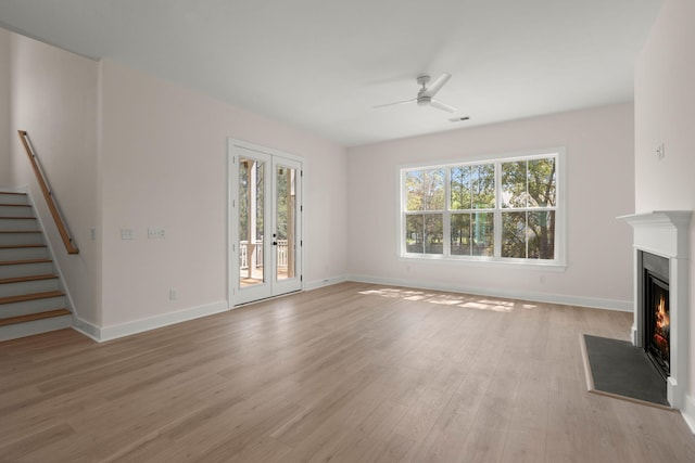unfurnished living room with stairs, a fireplace with flush hearth, baseboards, light wood finished floors, and ceiling fan