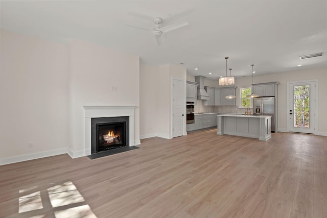unfurnished living room featuring a fireplace with flush hearth, light wood-style flooring, visible vents, baseboards, and a ceiling fan