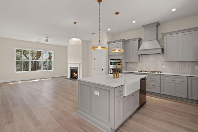 kitchen featuring custom range hood, gray cabinets, a fireplace with flush hearth, backsplash, and appliances with stainless steel finishes
