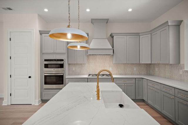 kitchen with premium range hood, gray cabinets, appliances with stainless steel finishes, and visible vents