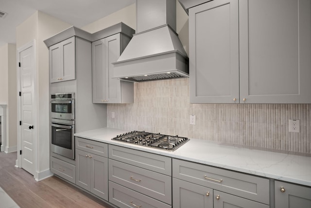 kitchen featuring decorative backsplash, light wood finished floors, stainless steel appliances, custom range hood, and gray cabinets
