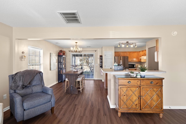 kitchen with a breakfast bar area, a textured ceiling, dark hardwood / wood-style floors, stainless steel fridge, and a notable chandelier