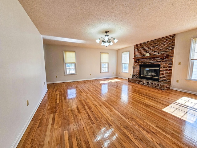 unfurnished living room with a fireplace, baseboards, an inviting chandelier, and wood finished floors